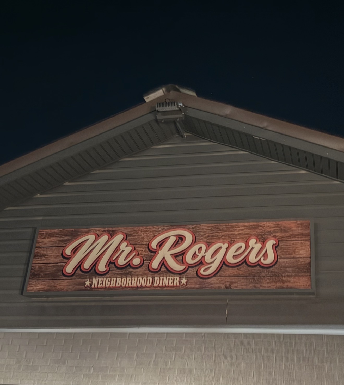 The Mr. Rogers Neighborhood Diner sign mounted on the restaurant, with cream script lettering outlined in red on a wood background